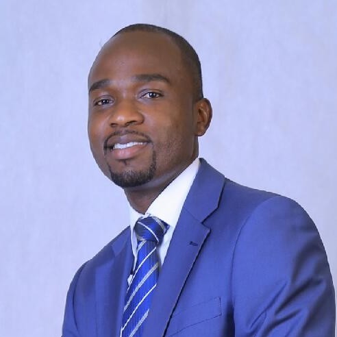 Portrait of Nassir Kuturamu, wearing a blue suit and striped-blue-white tie.