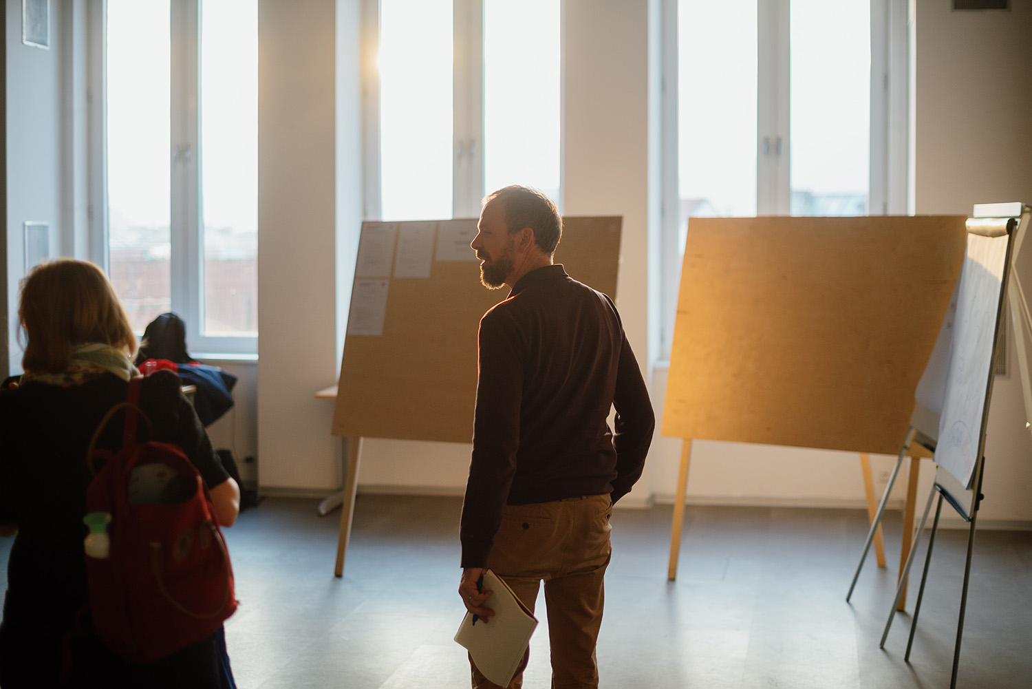 Participant of the Ashoka Visionary Program in CEE from behind, walking in coversation after the end of a session. Pinboards and a flipchart in the background.