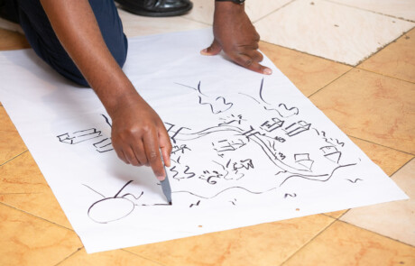 The program offers creative techniques like visualisig one's changemaker story. Image depicts the hands of a participant of the Ashoka Visionary Program, drawing a village ecosystem on a white flipchart paper.