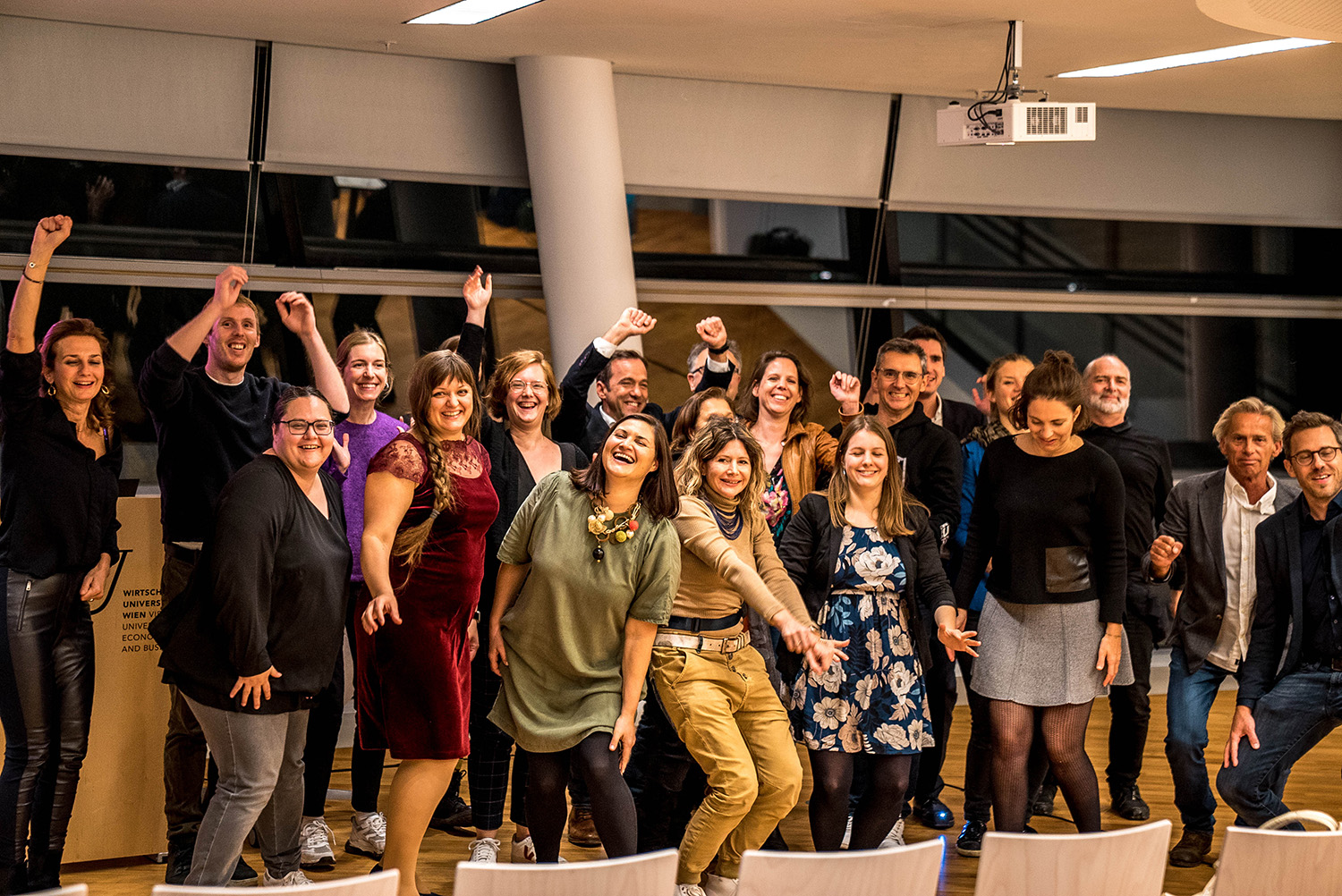 Grou picture of the opening of the Ashoka Visionary Program in CEE, in autumn 2021. Participants are standing up, in movements, raising their hands inside the WU University in Vienna.